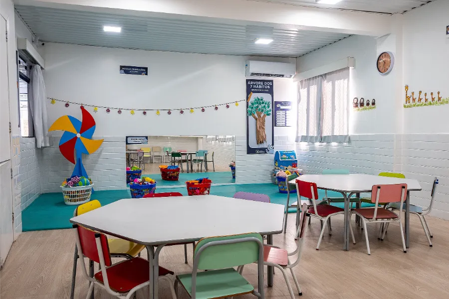 Sala da Educação Infantil do Colégio Atlântico com mesas coloridas e cantinho de brincadeiras, espaço que promove interação e aprendizado por meio do lúdico.