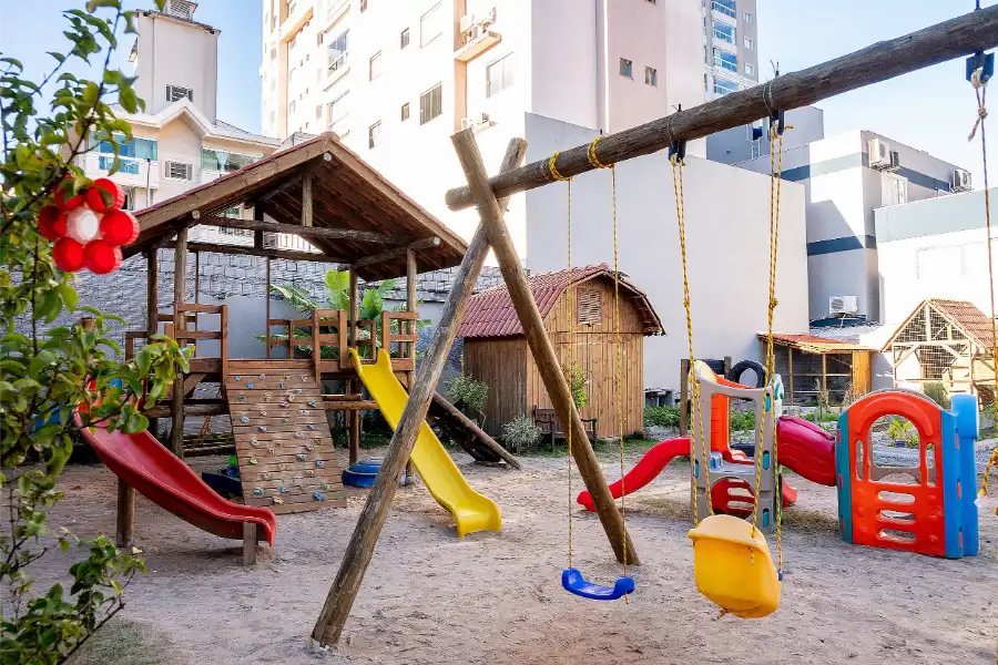 Playground externo do Colégio Atlântico com escorregadores, balanços e casinhas de madeira, espaço de recreação ao ar livre para as crianças.